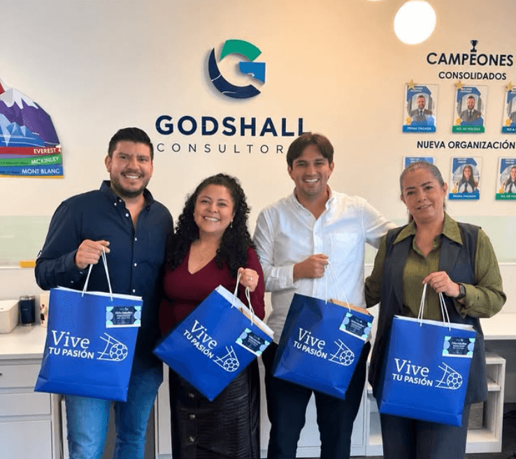 Equipo de asesores de Godshall Consultores en sus oficinas frente al muro con el logotipo y el tablero de campeones consolidados.